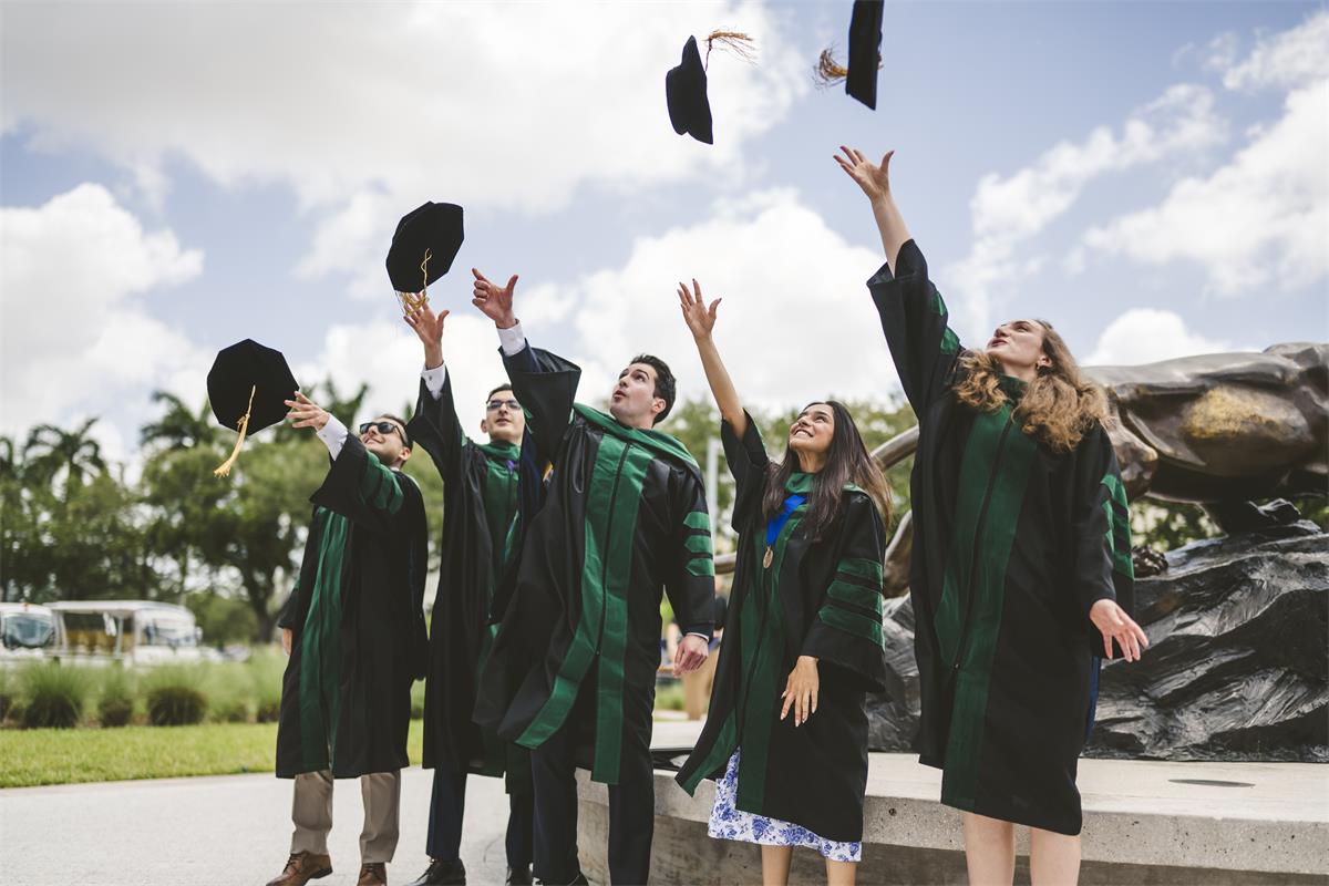 Five graduating students from FIU College of Medicine dress in regalia, throwing their tams in the air in celebration.